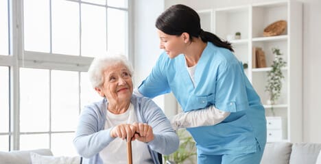 A nurse helping an elderly woman with her cane.